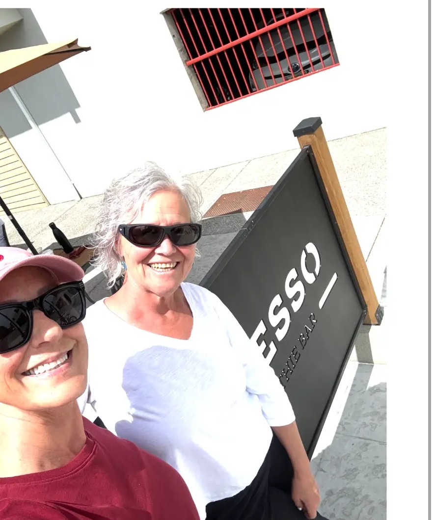 Cheryl and Nina smiling by the Impresso sign in Comox