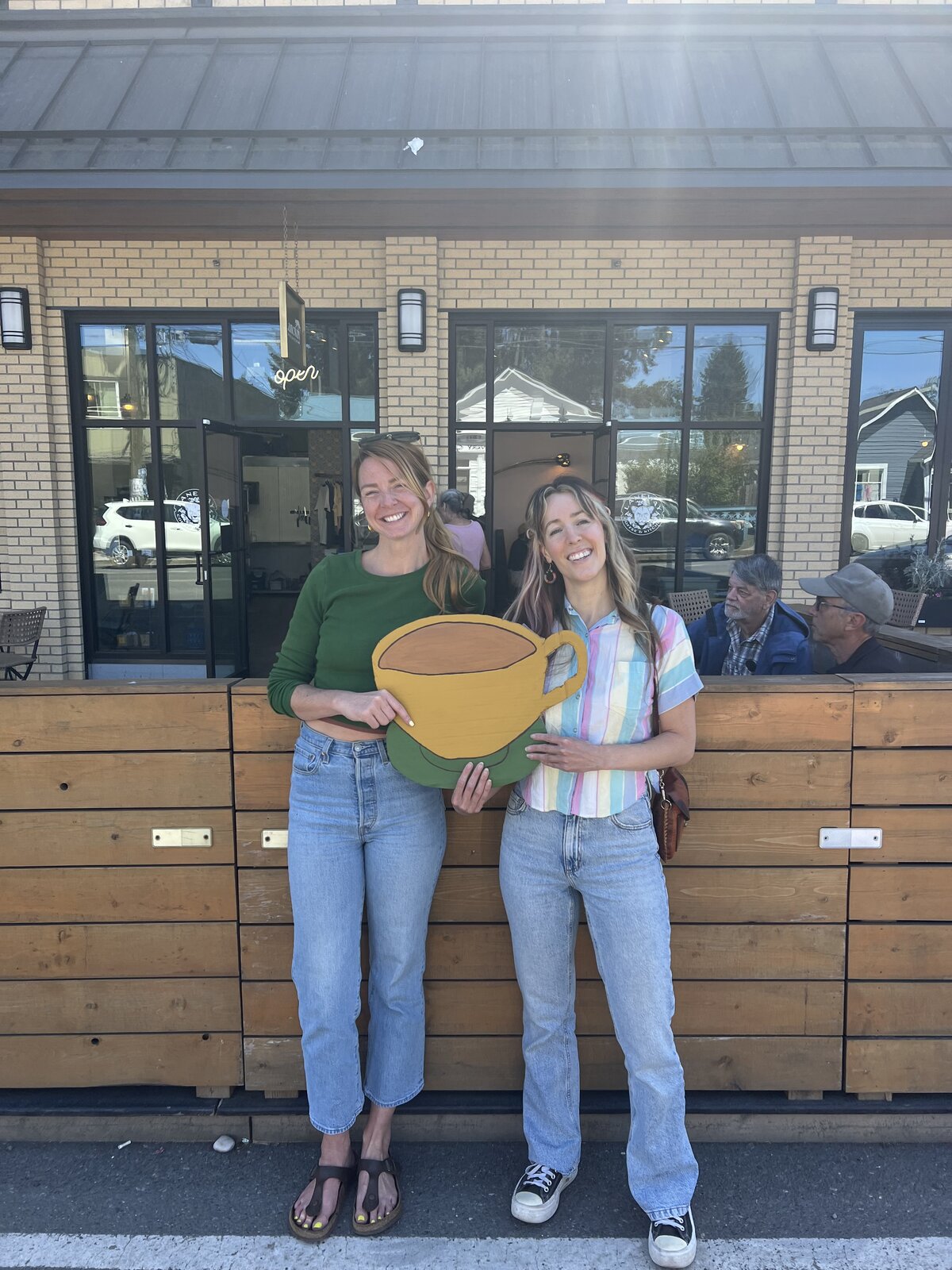 Maxine & Marie-Clo holding a hand-painted coffee cup outside Laneway in Cumberland